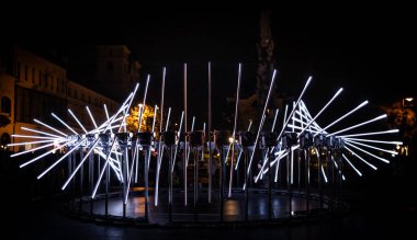 Büyüleyici gece sahnesi, mekâna fütüristik bir estetik ile hükmeden modern bir ışık tesisi yakalıyor ve geniş ışık spektrumunun ışınlarının sizi vurduğu dairesel bir formda çapraz dizilmiş birkaç tüp içeriyor.