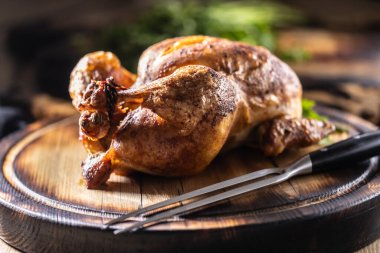 Altın kahverengiye kadar pişirilmiş bütün bir tavuk, ahşap bir kesim tahtasının üzerinde sunulur, taze maydanozla süslenir ve yanında bir et çatalı kırsal alanda sunulur..