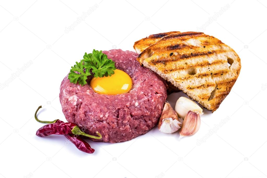 Tasty Steak tartare. Classic steak tartare over white. Ingredients: Raw beef meat salt pepper egg garlic chili herb decoration and toast bread. Isolated on white.
