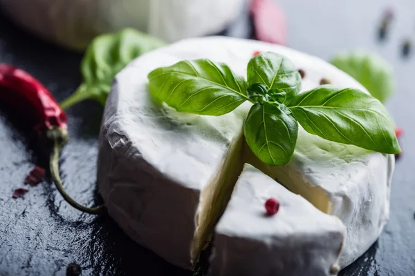 Verse Brie kaas en een segment op een granieten bord met basilicum bladeren vier kleuren peper en chili chilipepers. Italiaanse en Mediterrane ingrediënten. — Stockfoto