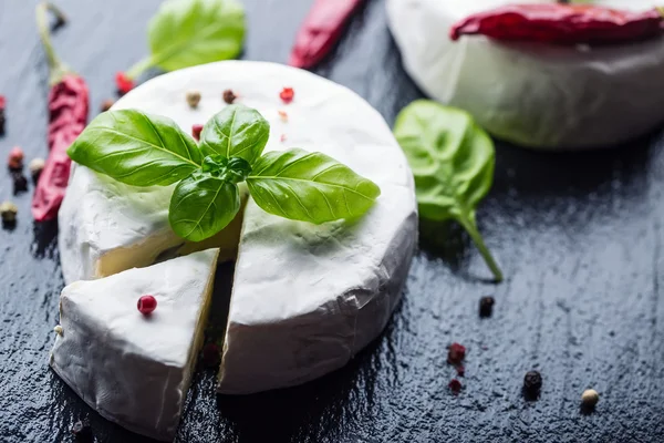Verse Brie kaas en een segment op een granieten bord met basilicum bladeren vier kleuren peper en chili chilipepers. Italiaanse en Mediterrane ingrediënten. — Stockfoto