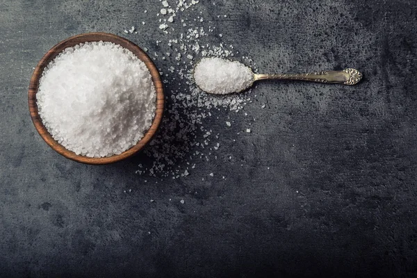 Salt. Coarse grained sea salt on granite - concrete  stone background with vintage spoon and wooden bowl — Stock fotografie