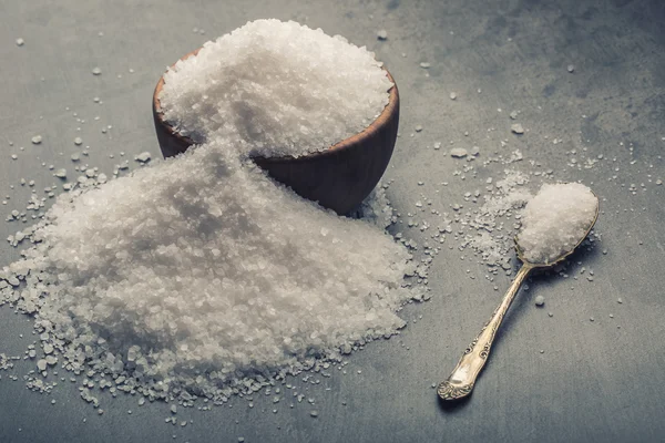 Salt. Coarse grained sea salt on granite - concrete  stone background with vintage spoon and wooden bowl — Stok fotoğraf