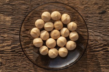 Kaba ahşap dokusunun arka planında şeffaf fincan tabağı üzerinde bir avuç makadamia fındığı..