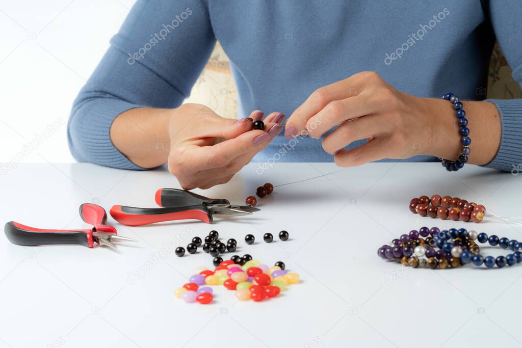 Jewelry making. Production bracelets and necklaces from multi-colored beads. Female hands with a tool on a white.