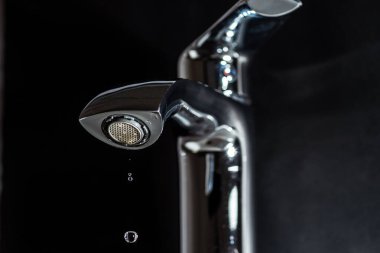 Musluktan temiz su damlatıyor. Karanlık bir arka planda.