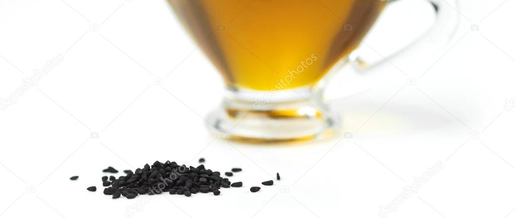 A handful of black cumin seeds on the background of a glass gravy boat with black seed oil. Selective focus. 