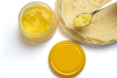 Gözleme yığınının yanında bir kaşık ve cam kavanozda Ghee. Beyaz bir arkaplanda izole edilmiş.