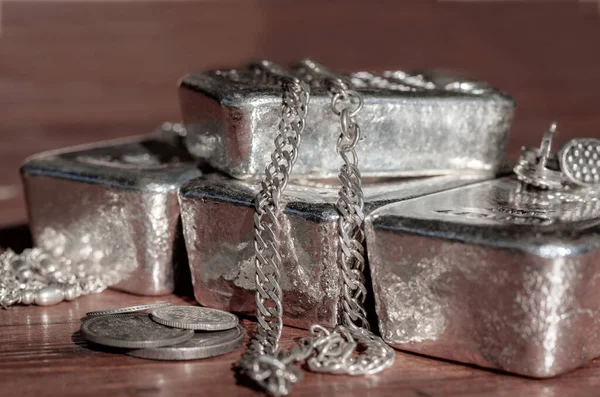 Silver bars, coins and jewelry on a brown background. Selective focus.