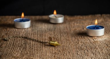 Zincirdeki sarkacın arka planında doğal bir kristal ve üç yanan mum var..