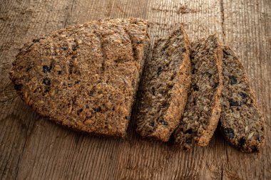 Tahta dokunun arka planında kepek, keten, kurutulmuş meyve, tohum, fındık ve diğer malzemelerden yapılan vejetaryen ekmeği..