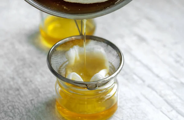 The oil is filtered into a glass jar through a metal sieve and cheesecloth.