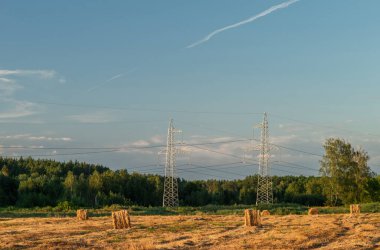 Hasat sonrası biçilmiş buğday tarlasında saman balyalarının yanında yüksek voltajlı elektrik hattı.. 