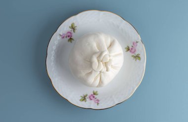 Porselen tabakta tipik bir İtalyan inek sütü Burrata peyniri kafası. Mavi bir arkaplanda