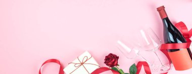 Sevgililer Günü tebrik kartı şablonu. Şarap şişesi, gözlük, kırmızı gül, hediye paketi ve kırmızı kurdeleli pembe arka plan. Uzayı kopyala Dümdüz yatıyordu, üst Wiew. Pankart