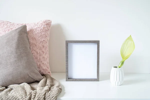 Beyaz masaya boş ahşap çerçeve modeli. Yumuşak renkli yastıklar, ekoseli vazo ve arum italikum çiçekli beyaz vazo. Modern ve asgari yaşam tarzı. İskandinav iç tasarımı