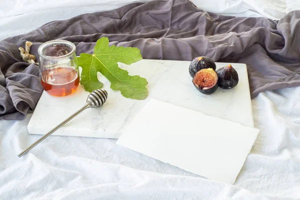 Autumn breakfast still life.Blank greeting card mockup, jar of honey and fig fruit on marble chop board.Breakfast in bed, fall food concept.Top view