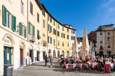 Lucca, İtalya-16 Şubat 2025: Güneşli bir günde Lucca 'nın ünlü amfitiyatro meydanında çeşitli yerlerde oturan insanlar