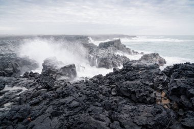 Bir bahar günü İzlanda 'daki Reykjanes Yarımadası' nda kara volkanik kayalar ve dalgalar kıyı şeridine çarpar..