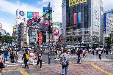 Tokyo, Japonya-Ağustos 7, 2024: Bir insan kalabalığı Ağustos 'un bir günü gökdelenler arasında renkli reklamlarla ünlü Shibuya Geçidi' ni geçiyor.