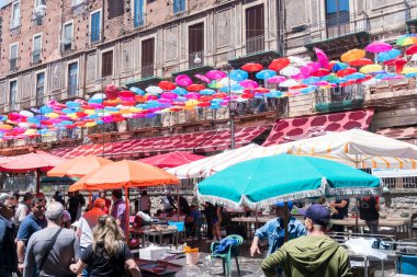 Catania, İtalya-14 Mayıs 2022: Bir bahar günü Catania pazarında balık tezgahları ve renkli şemsiyelerle sergilenen insanlar ve mallar