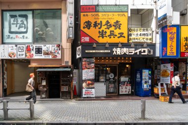 Tokyo, Japonya-Ağustos 7, 2024: İnsanlar Ağustos 'ta bir gün gökdelenler ve reklamlar arasında, Tokyo' nun Shibuya semtindeki renkli dükkanların önünden geçtiler.