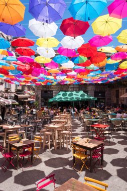 Catania, İtalya-14 Mayıs 2022: Bir bahar günü birçok renkli şemsiyenin gölgesi altında Catania 'daki barlarda oturan insanların dikey fotoğrafı