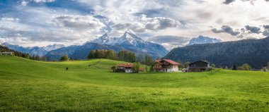 Idyllic alpine landscape with green meadows, farmhouses and snowcapped mountain tops clipart