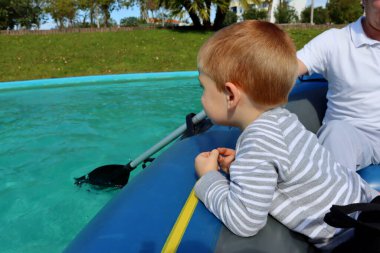 Üç yaşında bir çocuk lastik bir teknede oturur ve mesafeye bakar. Teknedeki sarışın bir çocuğun portresi.