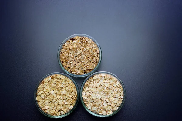 Yulaf ezmesi, arpa ve çavdar gevreği gri arka planda yuvarlak cam kaselerde..