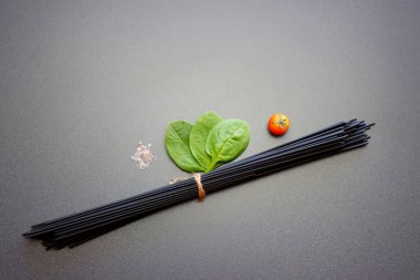 Siyah spagetti, ıspanak, vişneli domates ve gri arka planda pembe tuz..