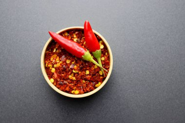 Yuvarlak bir kasede kırmızı biber taneleri ve tohumlar ve gri arka planda iki taze biber..