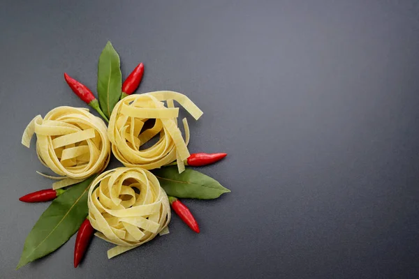 Sarı makarna tagliatelle, kırmızı biber kabukları malagatta ve gri arka planda yeşil defne yaprakları..