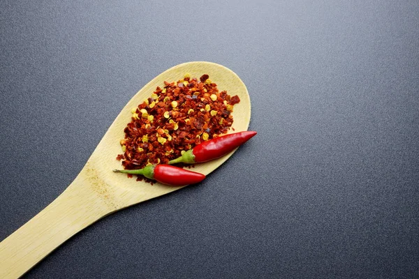 Ahşap kaşıkta kırmızı biber taneleri ve tohumları ve gri arka planda iki taze malagueta biberi..