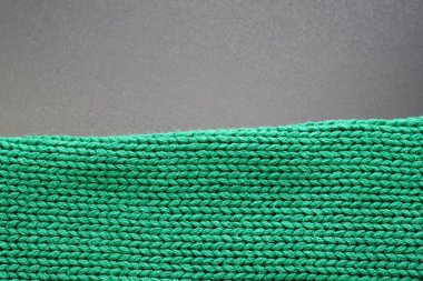 Gri bir arka planda zümrüt renginde kalın örülü bir süveterin dokusu. Doku, arkaplan, desen, örgü tasarımı.