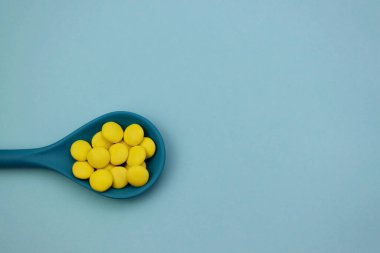 Açık mavi arka planda mavi kaşıkta sarı tatlı damlalar.