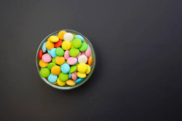 Multicolored sweet candies in a round bowl on a gray background.