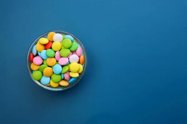 Multicolored sweet candies in a round bowl on a blue background.