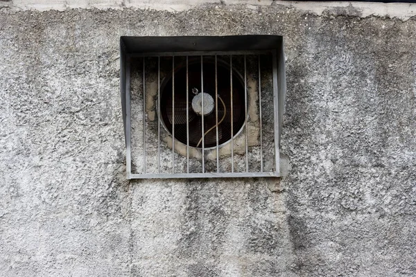 An old exhaust fan installed in the wall of a gray building.