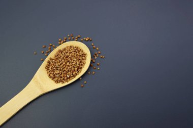 Gri arka planda tahta kaşıkta karabuğday.