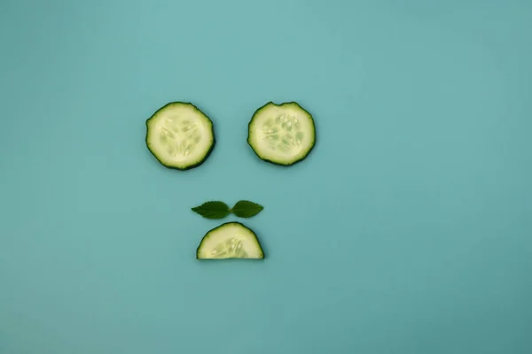 Circles and semicircles of a cucumber with green mint leaves on a light blue background. Funny background.