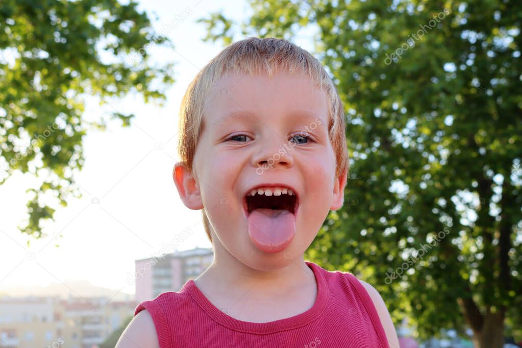 A four-year-old cute boy sticks out his tongue. Portrait of a blond cocky boy.