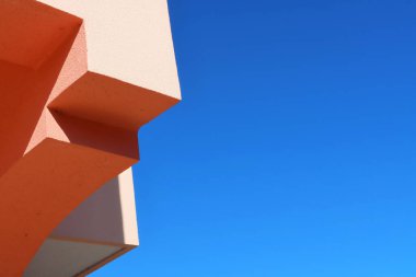 Açık mavi gökyüzüne karşı şeftali ve turuncu renkli cesur geometrik şekillere sahip minimum soyut mimari, güçlü güneş ışığı ve gölgeler kopyalama alanı ile temiz modern minimalist kompozisyon yaratıyor..