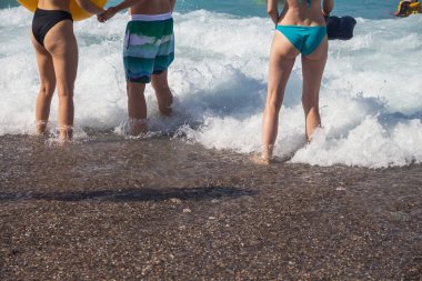 Yaz tatilleri ve deniz tatilleri, yüzme şortu ve mayo giyen insanlar, deniz dalgalar halinde dalgalar halinde insanların ayaklarına vuruyor, sahilde, insanlar ve okyanus, insanların ayakları ve okyanus.