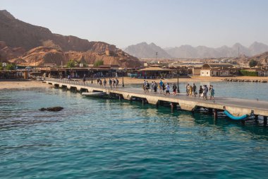 Mısır, 4.10.2025 - Kızıldeniz 'in turkuaz sularına doğru bir beton iskele uzanıyor ve turistler bu yolda yürüyor. Watanya yat limanı, turistleri taşıyan yatların dalış için ayrıldığı yer. Mısır 'a Gezinti.