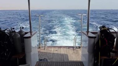 Yatın arka tarafında, denizde dolaşırken. Motor spreyi kıç tarafının arkasında görünür ve dalış teçhizatı ve tanklar yanlara yerleştirilmiştir. Atmosfer, denizde macera ve özgürlüğü çağrıştırıyor..