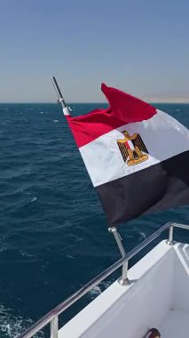 Mısır bayrağı denizde yelken açan bir yatta dalgalanıyor. Kamera yatın uyanışına doğru sorunsuzca kayıyor ve su sıçrıyor. Uyan..