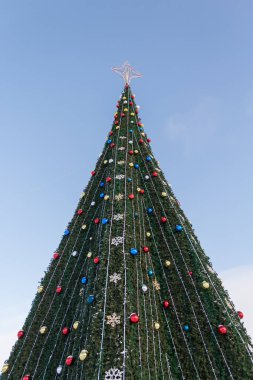 Şenlikli süslemeleri olan bir Noel ağacı ve mavi gökyüzünün tepesinde bir yıldız..