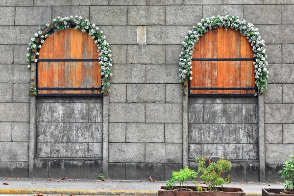 Arched boarded up windows with wooden shutters-white roses garlands-concrrete masonry units or CMUs wall facing General Luna St.-stop for e.trikes covering the whole Intramuros-Inner Walled City area.