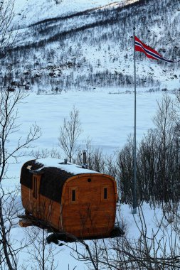 Langvatnet Gölü 'nün N.sahilindeki kulübenin ahşap saunası. S.shore' daki Tverrelf Tindan Dağı 'na bakıyor. Norveç bayrağı sallanıyor. Kvaefjord Kommune-Troms Fylke-Hinnoya-Vesteralen-Norveç.